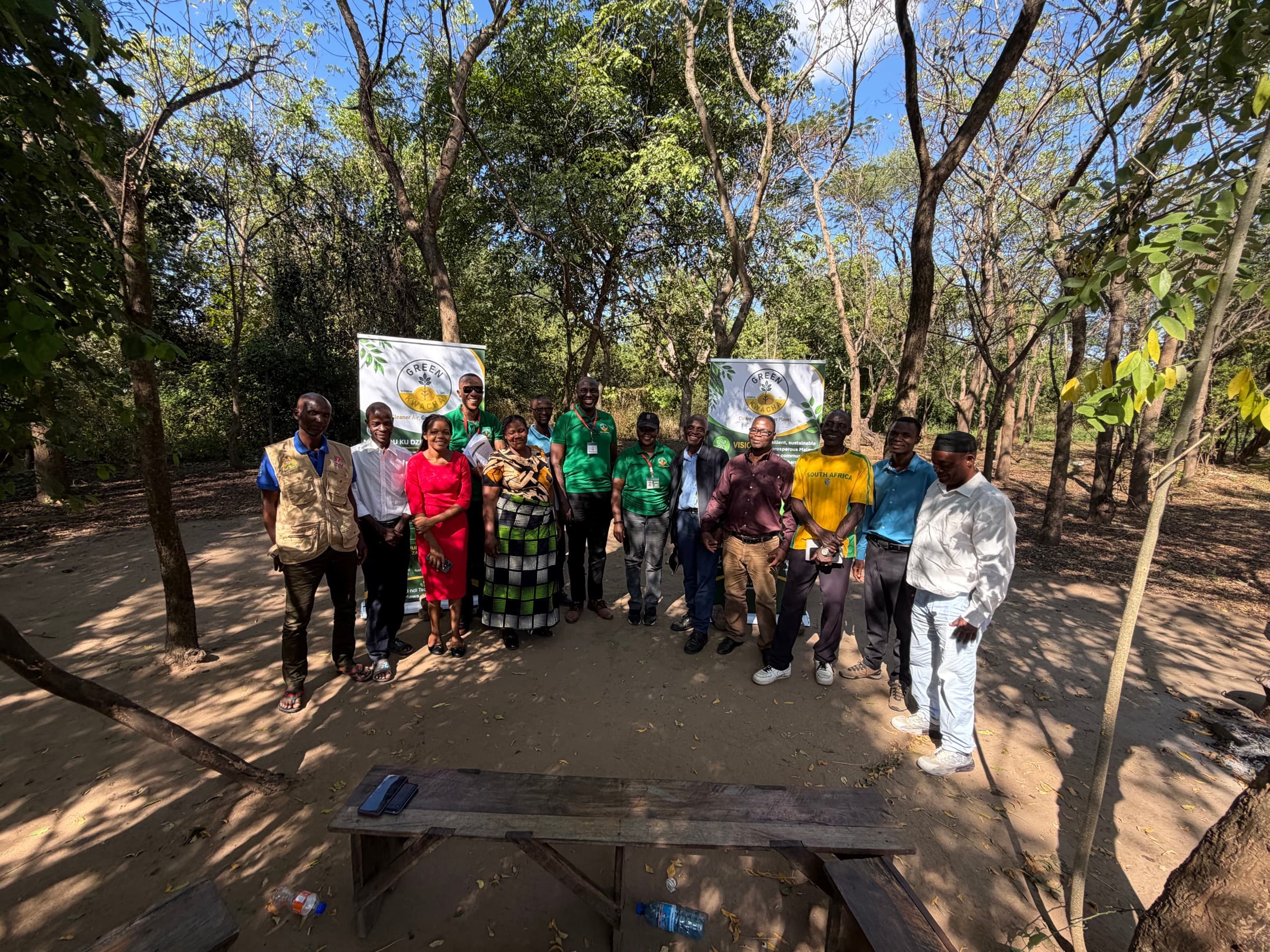 The GreenKwacha team and community members together under trees, some holding printed visual-aid boards.