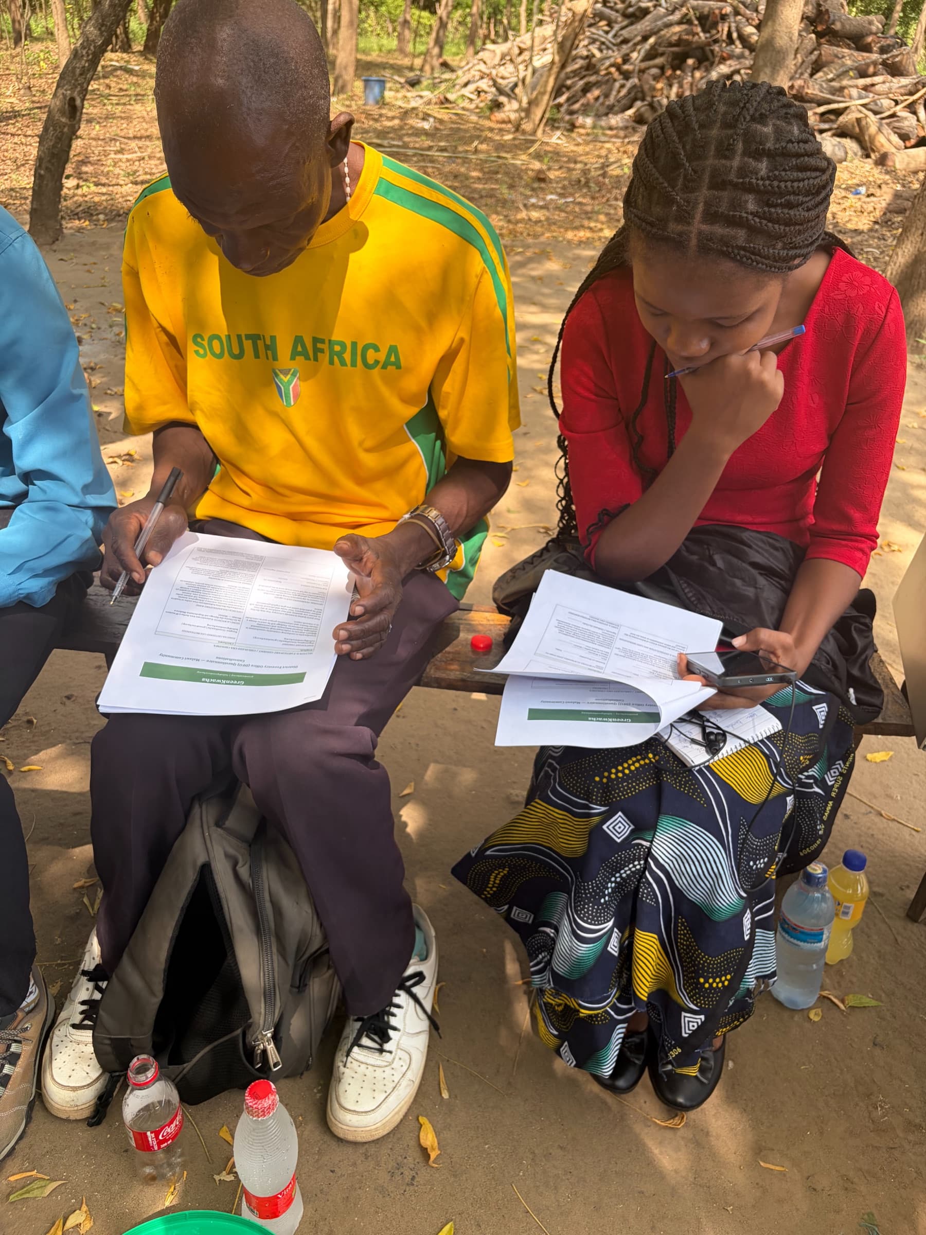 Two young people in GreenKwacha tee-shirts filling in the community consultation questionnaire by hand.
